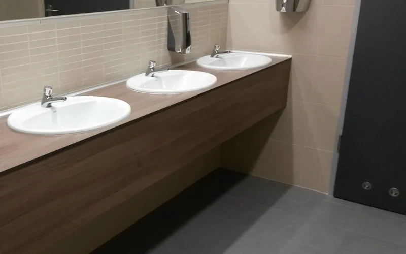 Wood-grain vanity top with three basins in a washroom