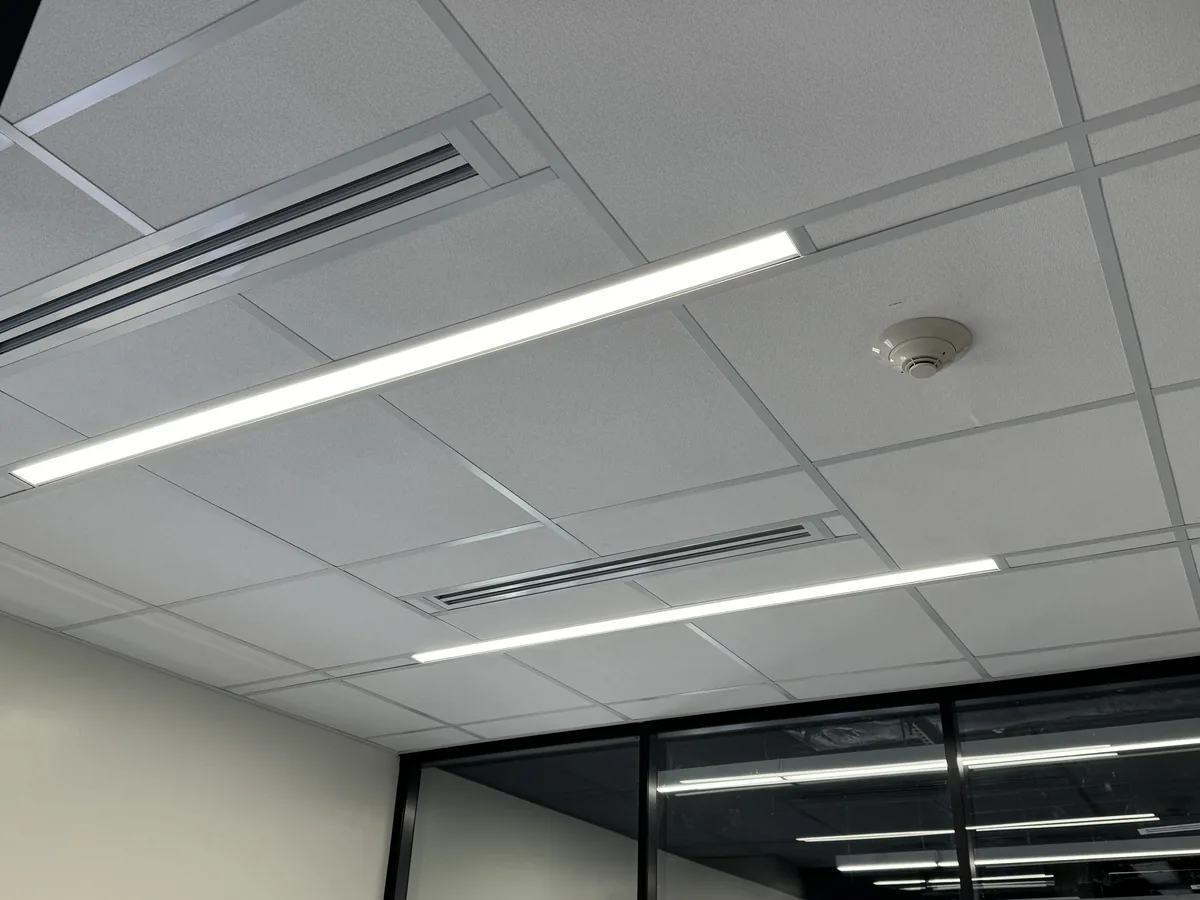 Lay-in ceiling tiles on an exposed grid with linear lights, two slot diffusers and a smoke detector