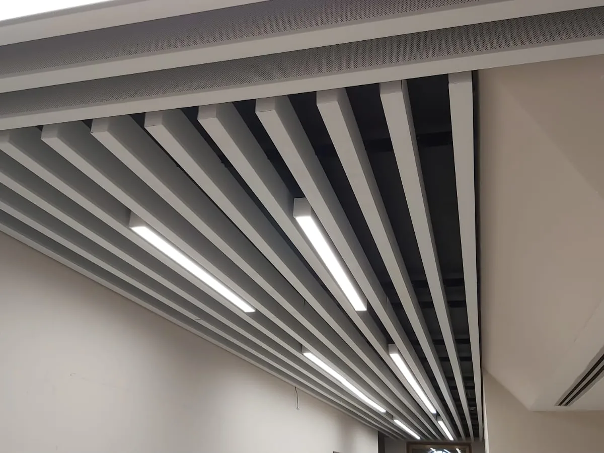 Close view of baffle blades with linear lights and a fabric-edged trim panel along the top