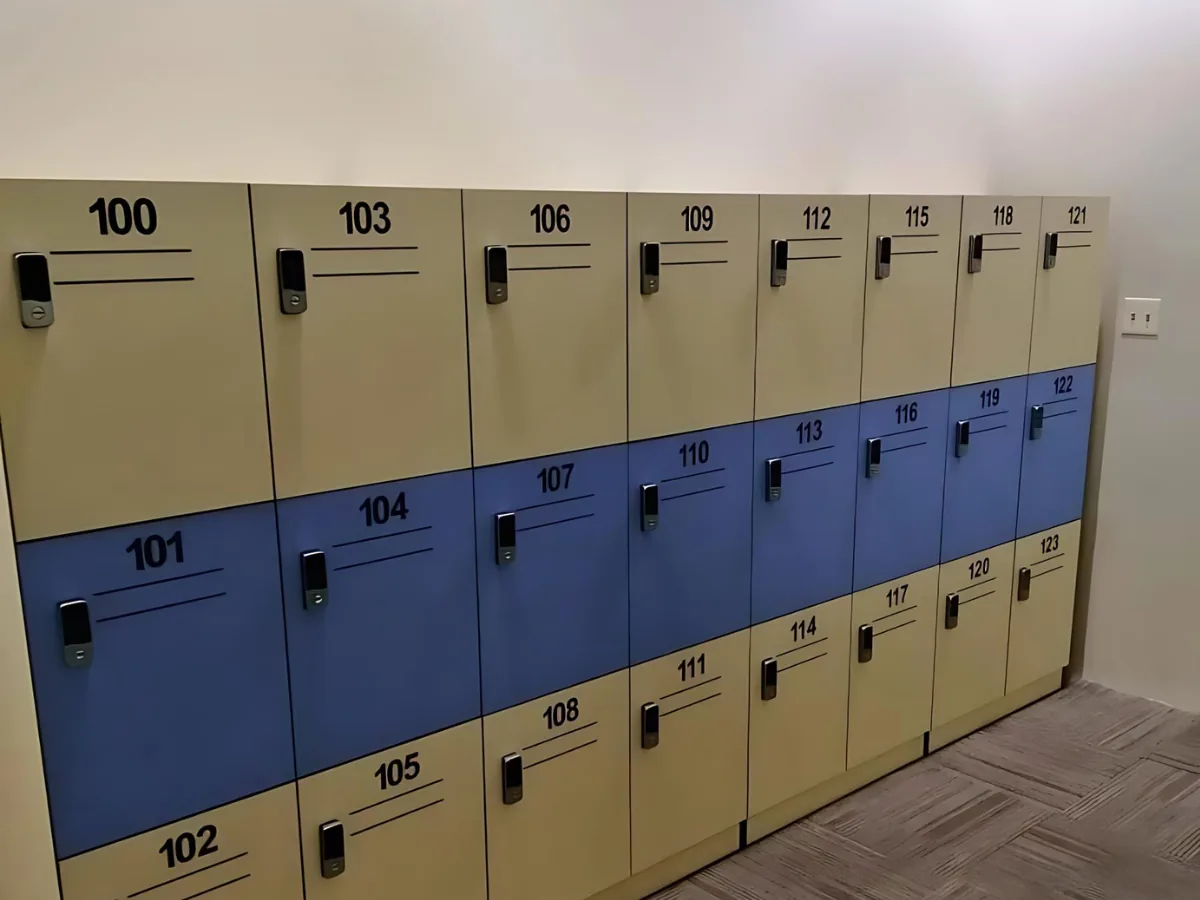 Three-tier locker bank in beige and blue with numbered doors and keypad locks over a carpet-tile floor