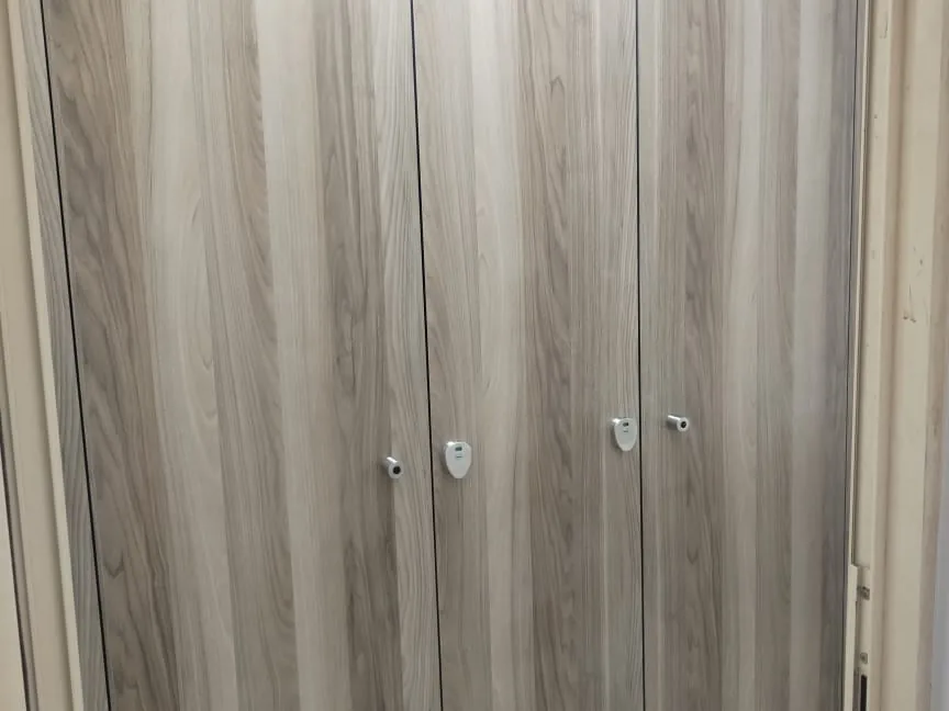Close view of three wood-grain cubicle doors with metal turn locks and occupancy indicators