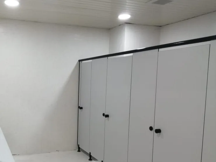 Light-grey toilet cubicles with black knobs under a black headrail, on metal legs