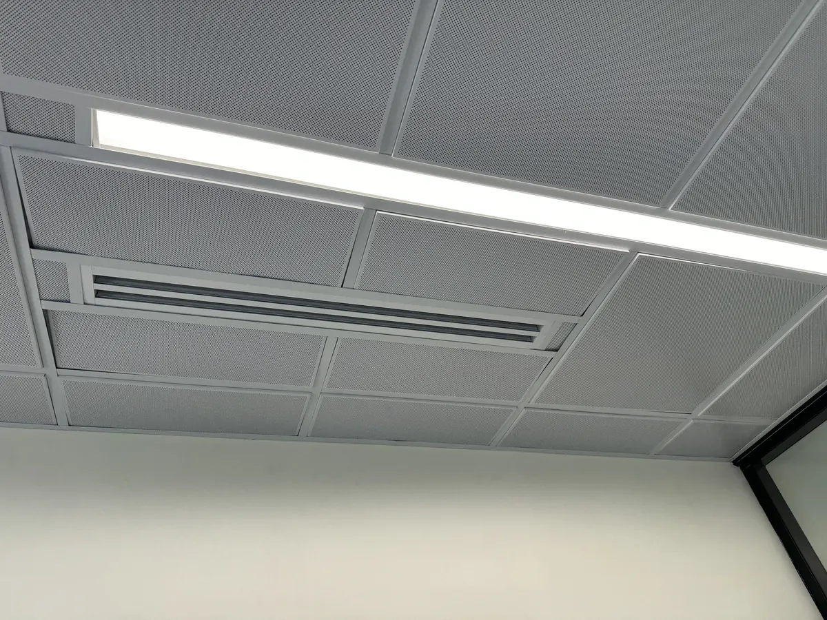 Perforated metal ceiling tiles on a light grid with a linear light and a slot diffuser, above a white wall