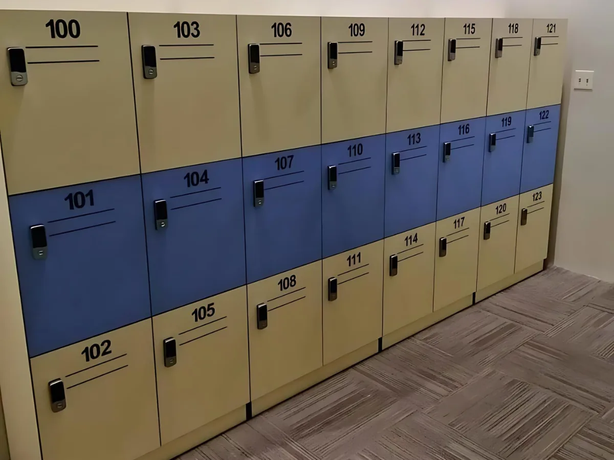 Three-tier locker bank in beige and blue, each numbered door fitted with an electronic keypad lock, on a carpet-tile floor