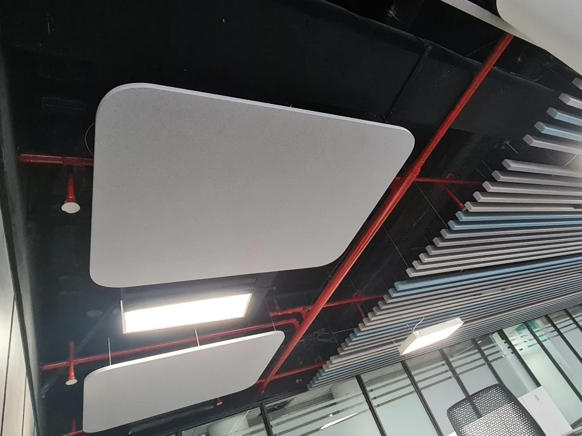 Two rounded white acoustic clouds hung below an open black soffit with red sprinkler pipes, beside a run of baffles