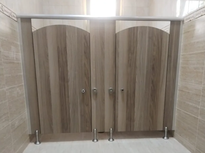 Two arched-top wood-grain cubicle doors between pilasters under a metal headrail, on metal legs, in a tiled washroom