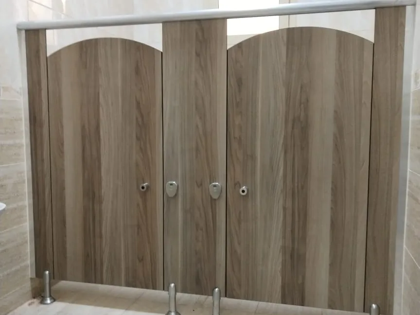 Two walnut-look toilet cubicles with arched door tops under a round metal headrail, on metal legs