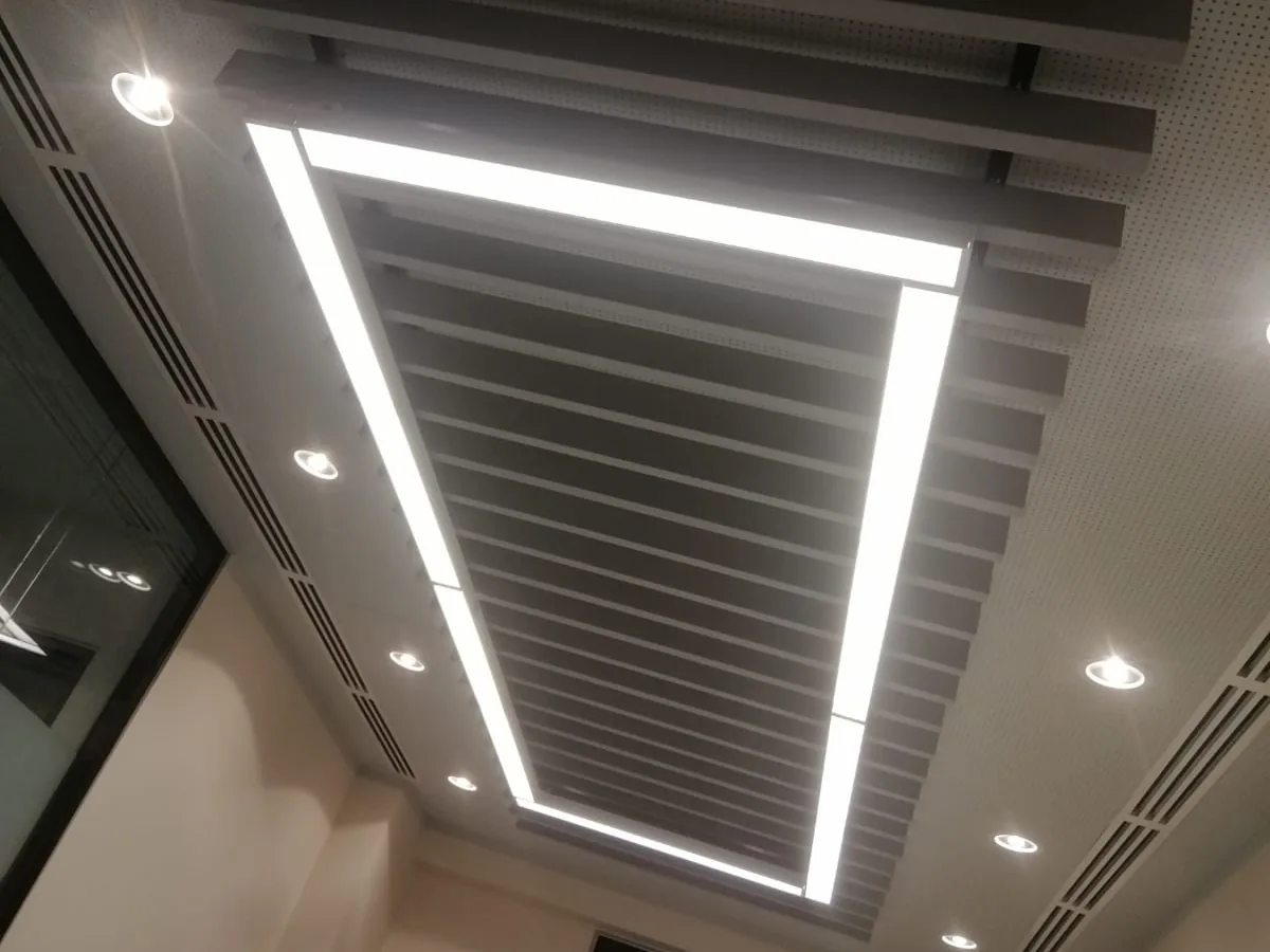 مستطيل من شرائح بافل داكنة يحيط به خط إنارة LED متصل، داخل سقف مثقّب مع إنارة سقفية غائرة