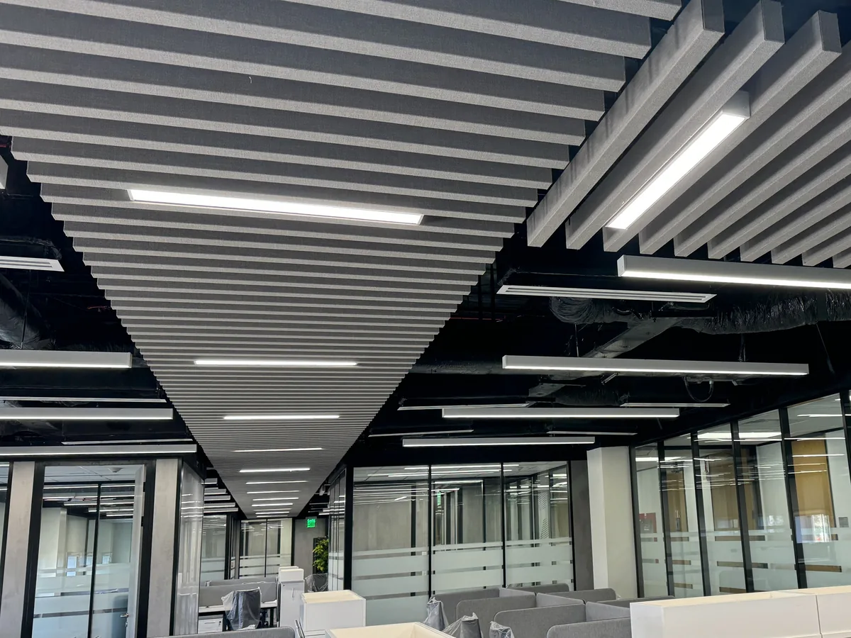 Two grey baffle canopies with linear lights under an open soffit, above glass-fronted offices