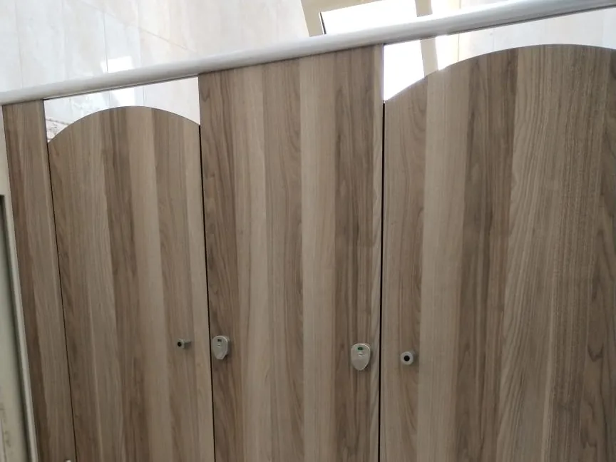 Three wood-grain toilet cubicles with arched door tops under a round headrail