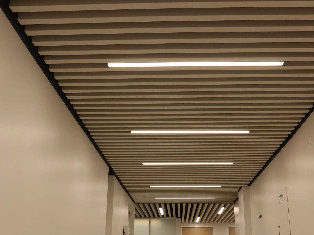 Long corridor whose ceiling is a run of closely spaced linear baffles with strip lights between them