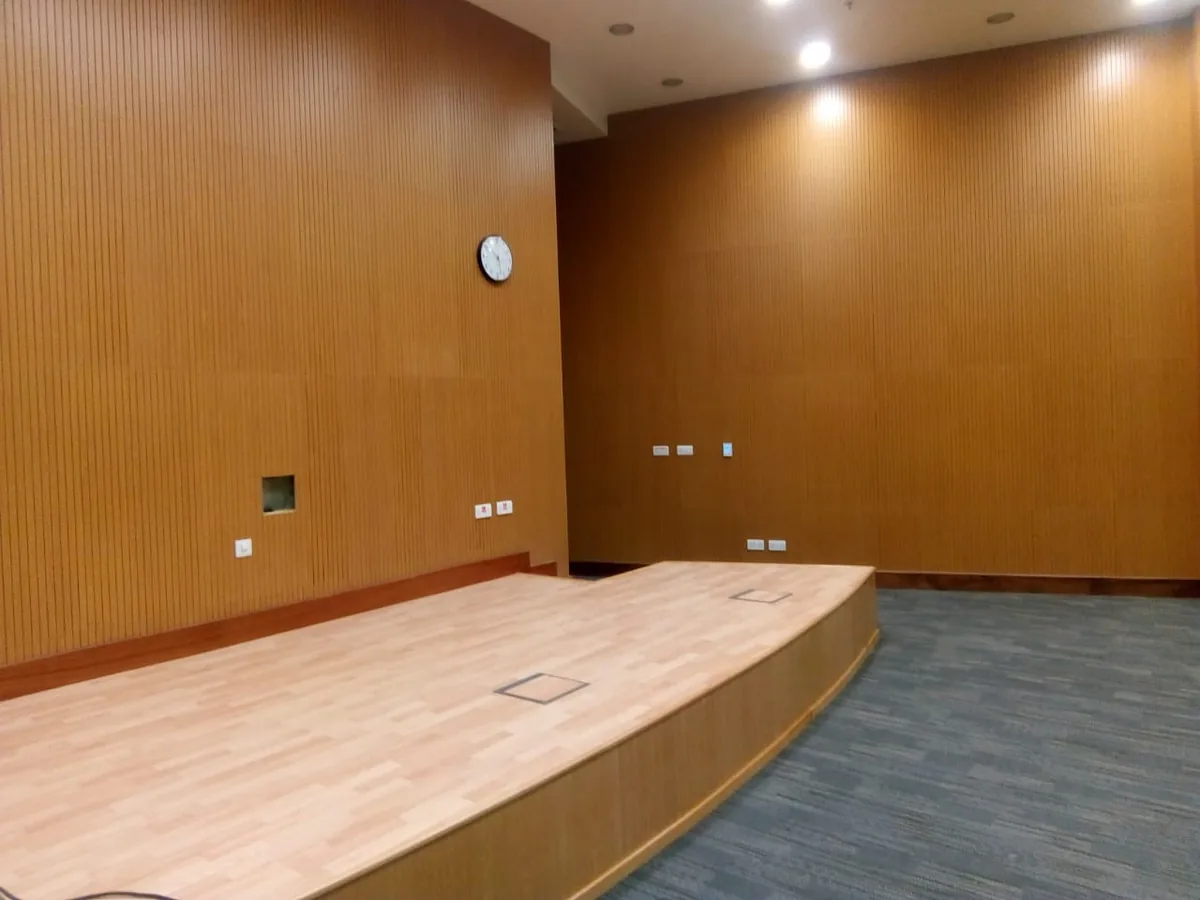 Raised stage with a wood-look floor in front of full-height grooved wall panels and a wall clock