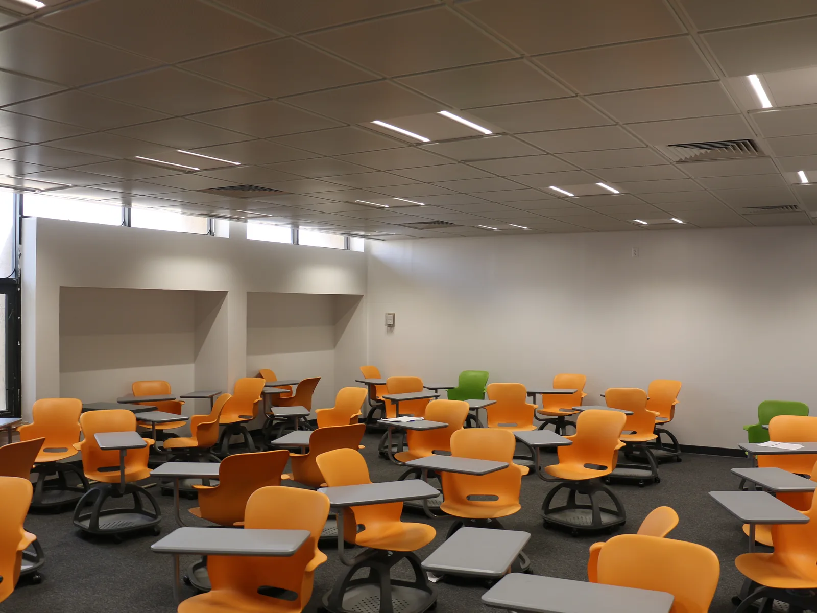 Classroom with a lay-in tile ceiling, linear lights and a carpet floor