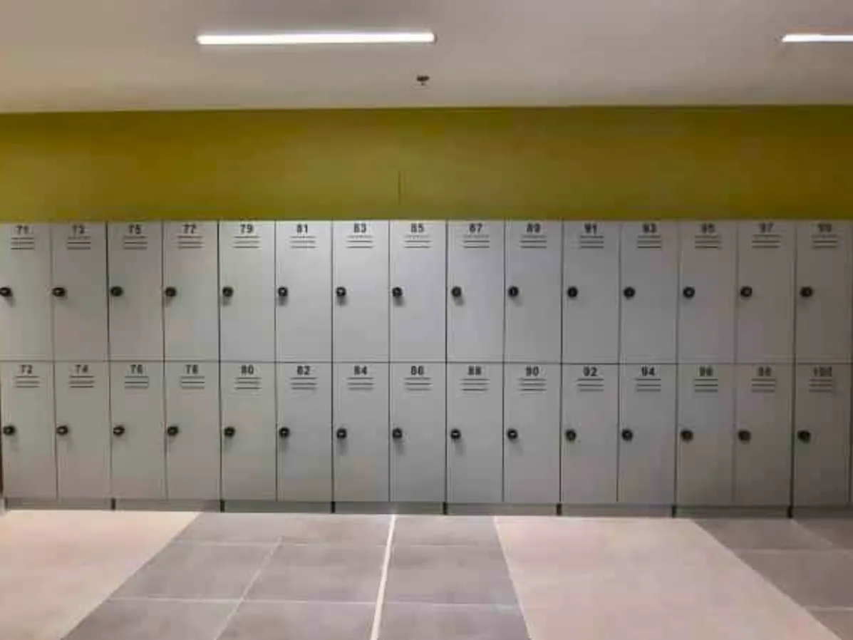 Long run of grey two-tier lockers with numbered doors against an olive-green wall