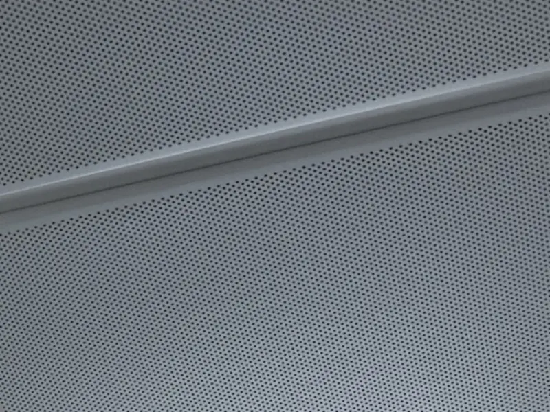 Close view of perforated metal ceiling tiles meeting at a grid tee