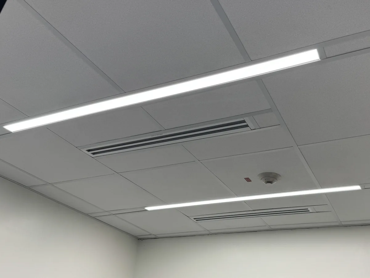 Lay-in ceiling tiles on an exposed grid with two linear lights, slot diffusers and a smoke detector