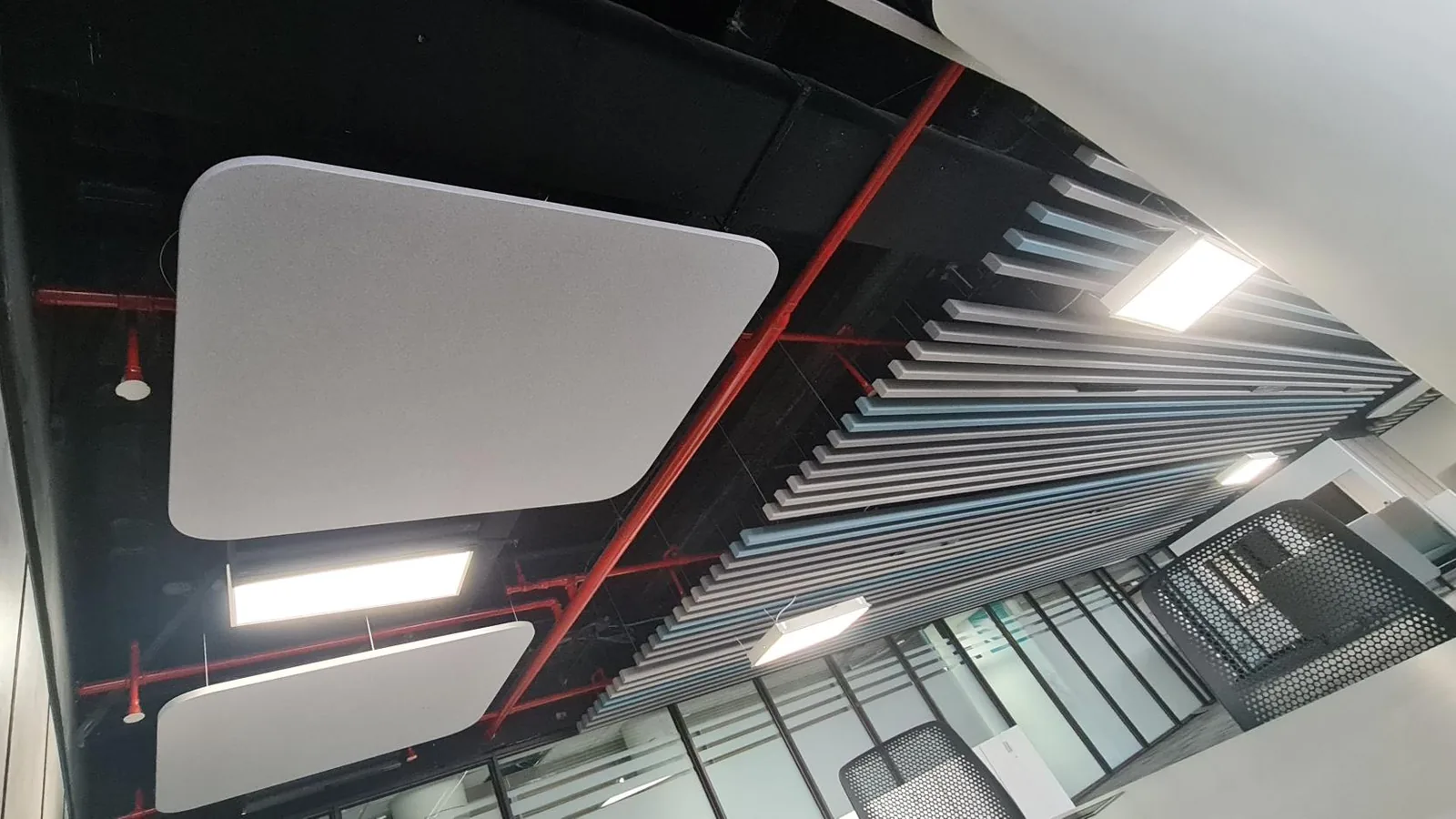 Flat acoustic raft panels suspended below an open, black-painted soffit beside a baffle ceiling