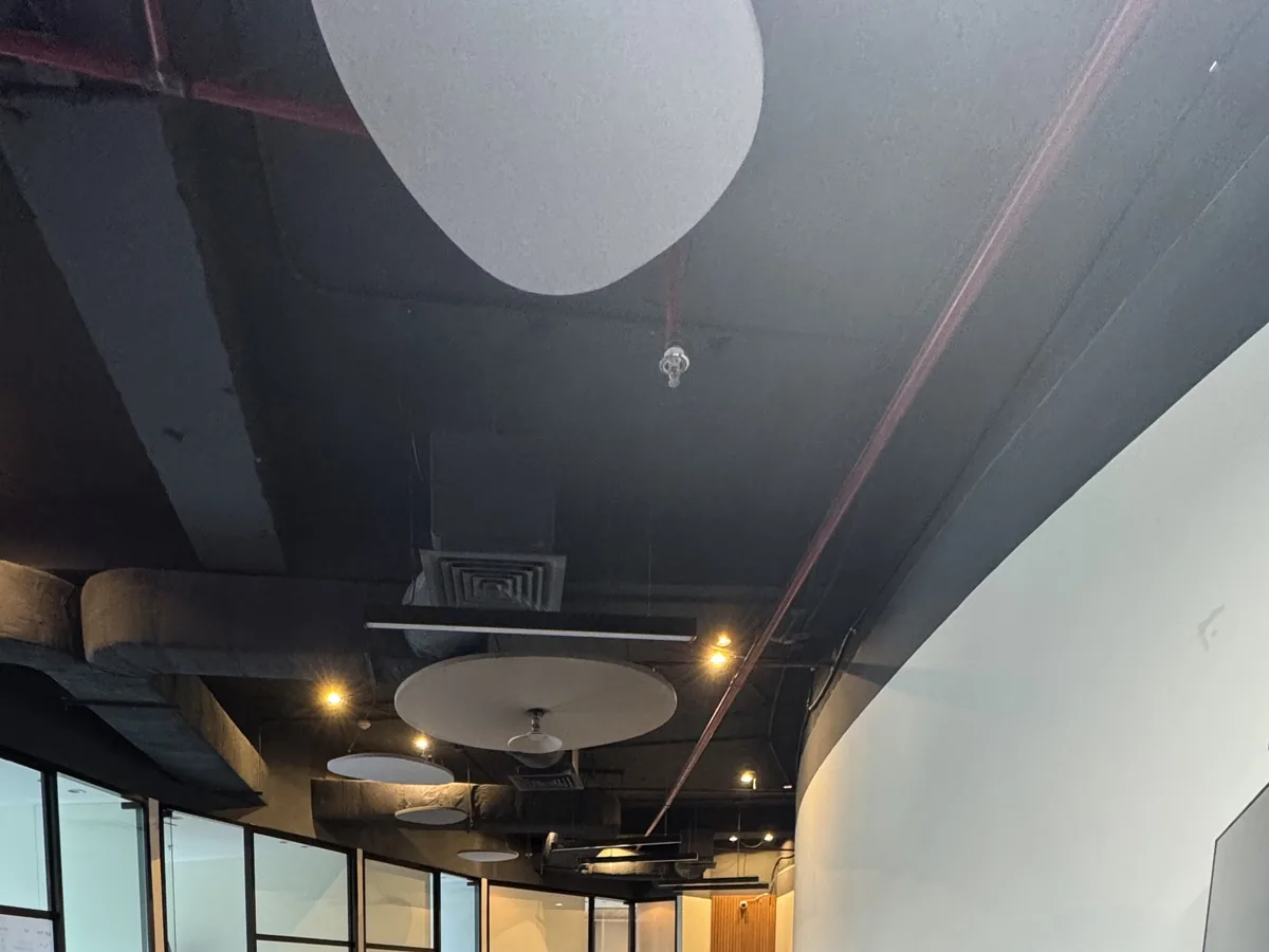 Round acoustic clouds suspended at different heights below an open soffit with exposed ducts