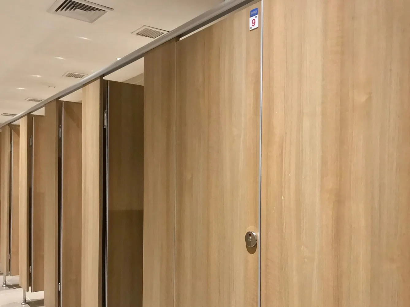 Light-oak toilet cubicles along a washroom corridor, with numbered doors and flush door locks