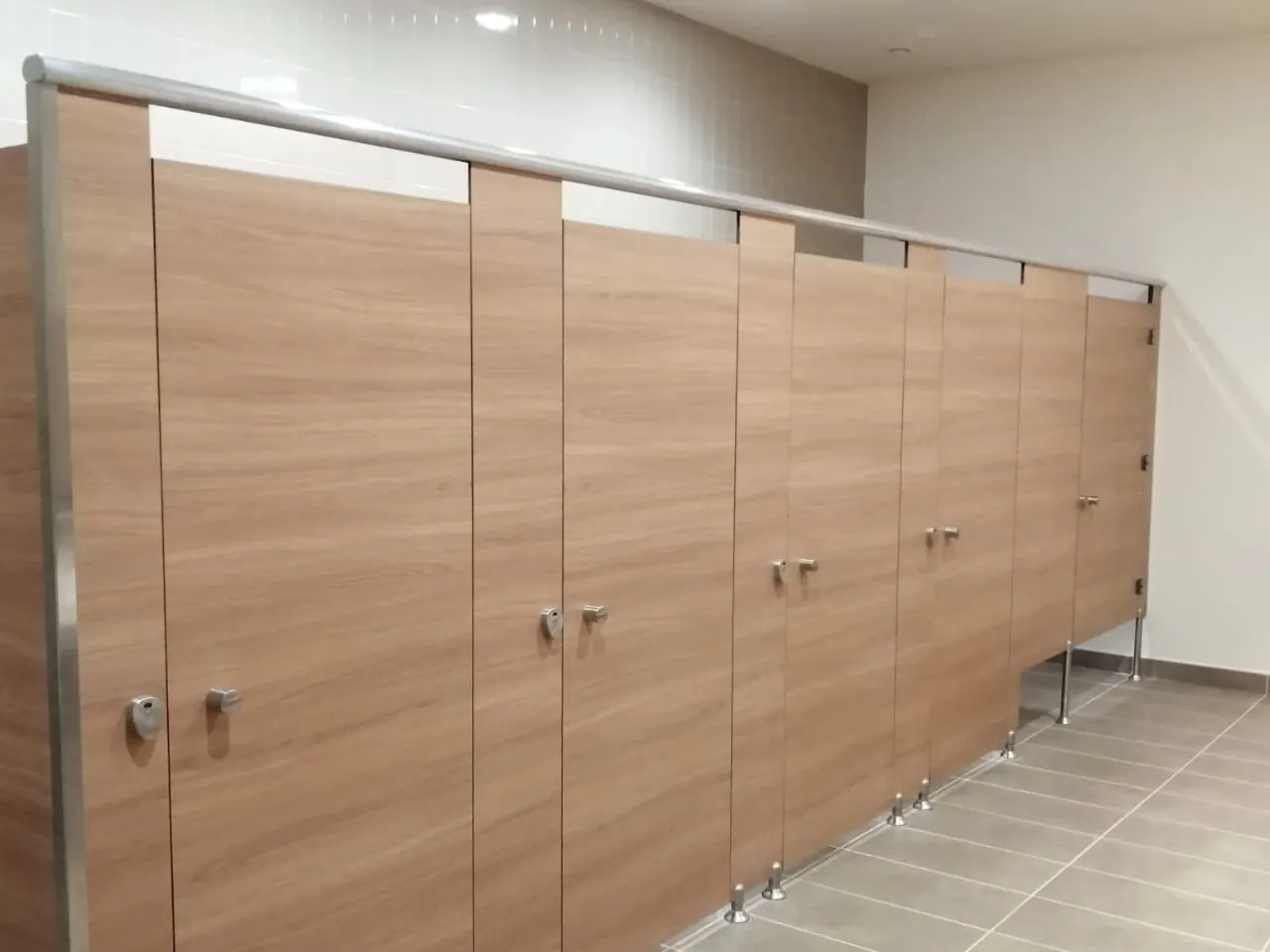 Wood-grain toilet cubicles under a continuous headrail, on adjustable legs