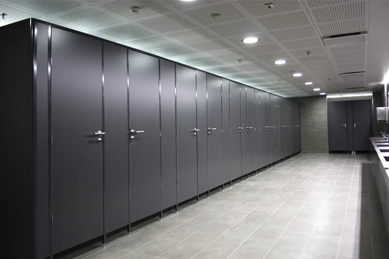 Long run of tall dark-grey toilet cubicles with lever handles along a tiled washroom