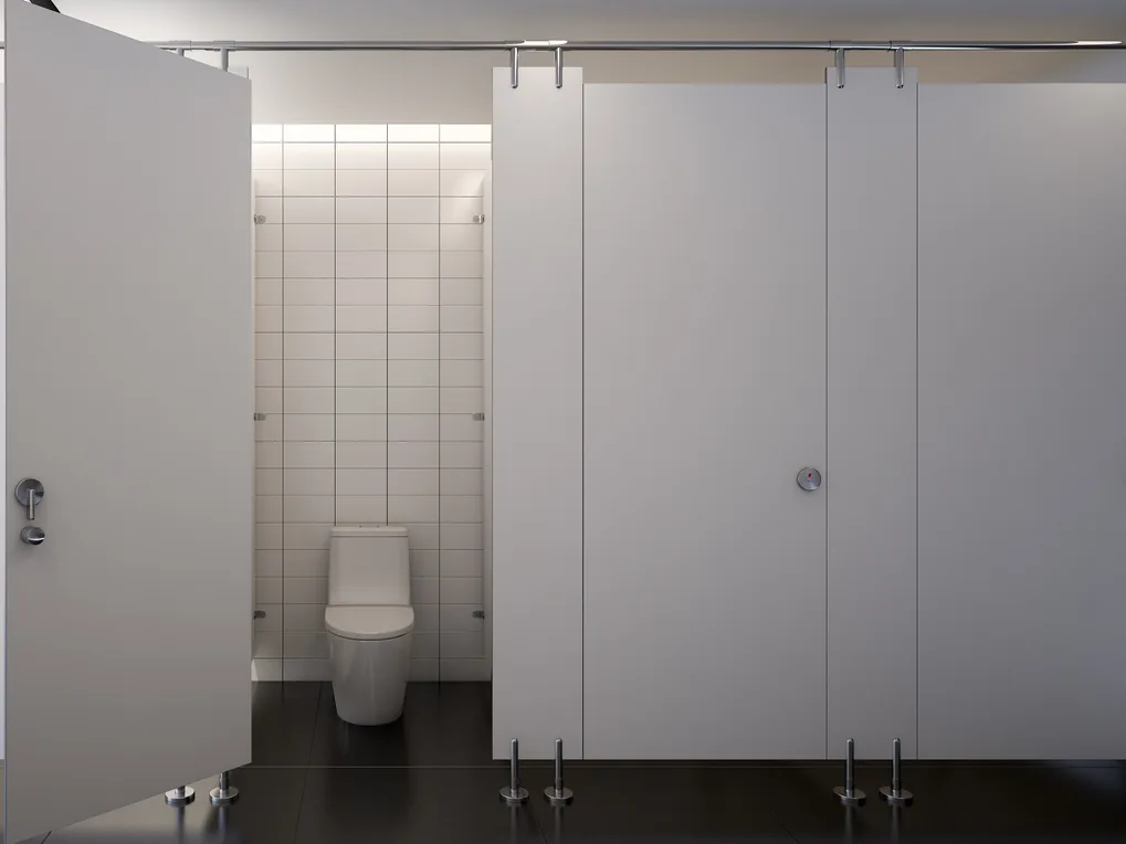 White toilet cubicles on metal legs under a continuous headrail, with one door open